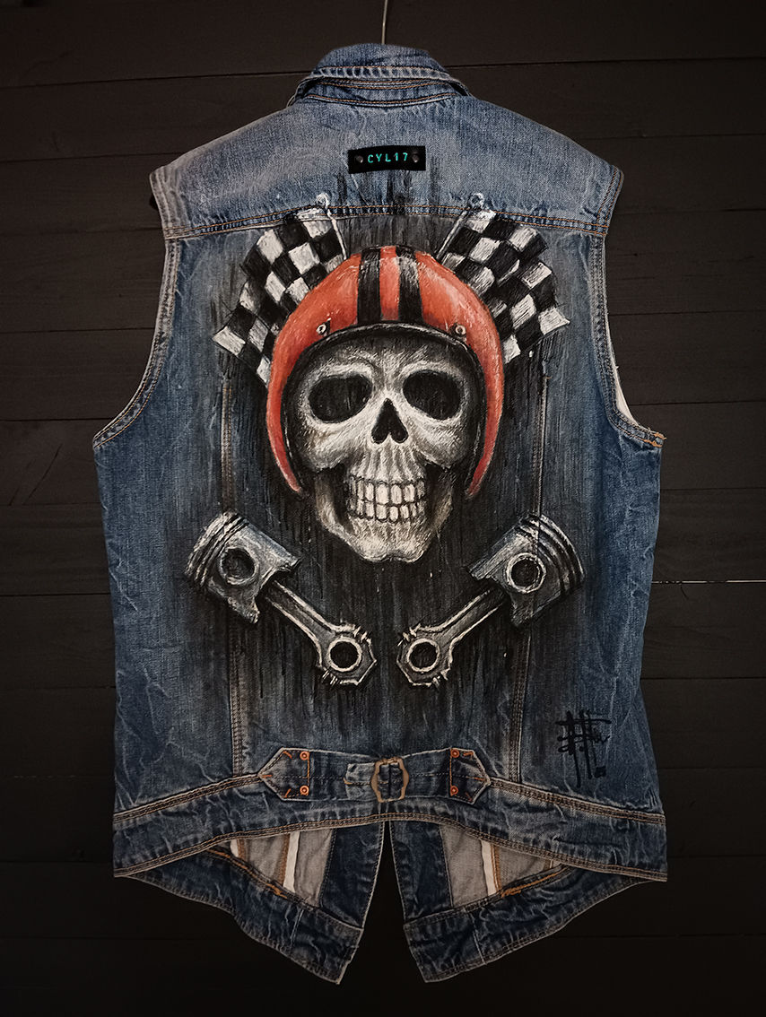The back of a vintage denim waistcoat featuring a hand-painted illustration of a skull wearing an orange helmet, chequered flags and two pistons, in an artistic, worn-in style.