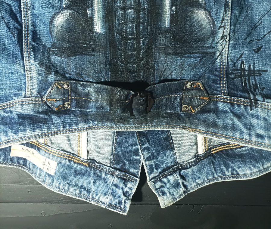 The back of a vintage denim waistcoat featuring a hand-painted illustration of a biker riding a motorbike, in an artistic, worn-in style.