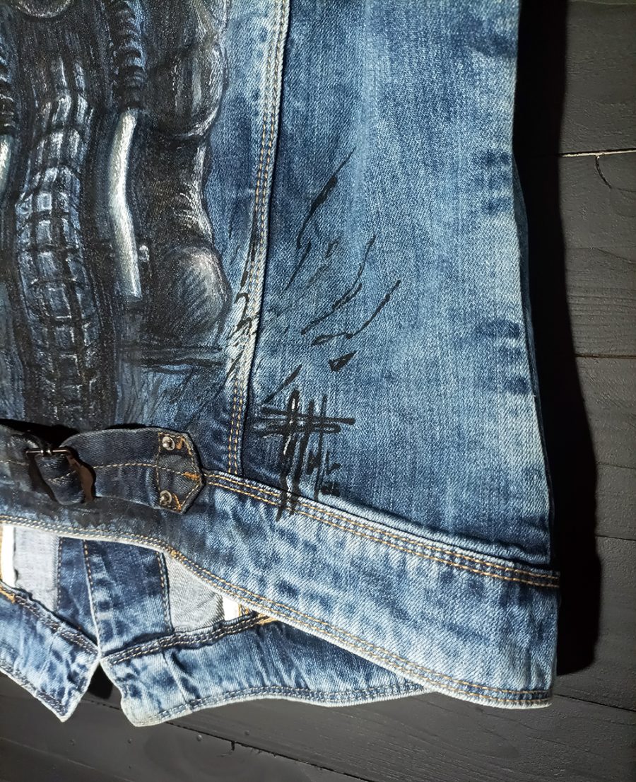 The lower part of a vintage denim waistcoat featuring a hand-painted illustration of a biker riding a motorbike, in an artistic, worn-in style.