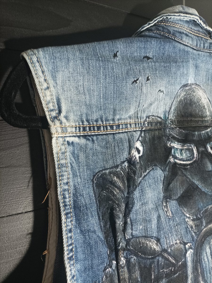 The back of a vintage denim waistcoat featuring a hand-painted illustration of a biker riding a motorbike, in an artistic, worn-in style.