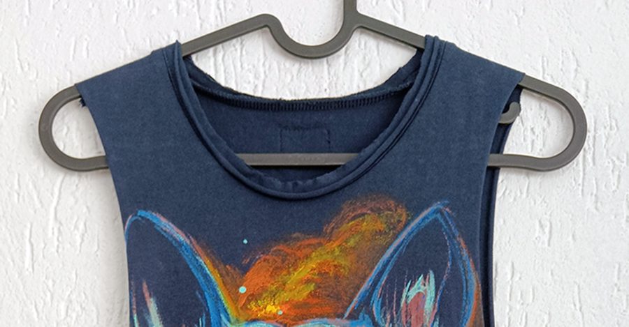 Detail of the round neckline and the upper part of the hand-painted design depicting the ears of a French bulldog on blue fabric