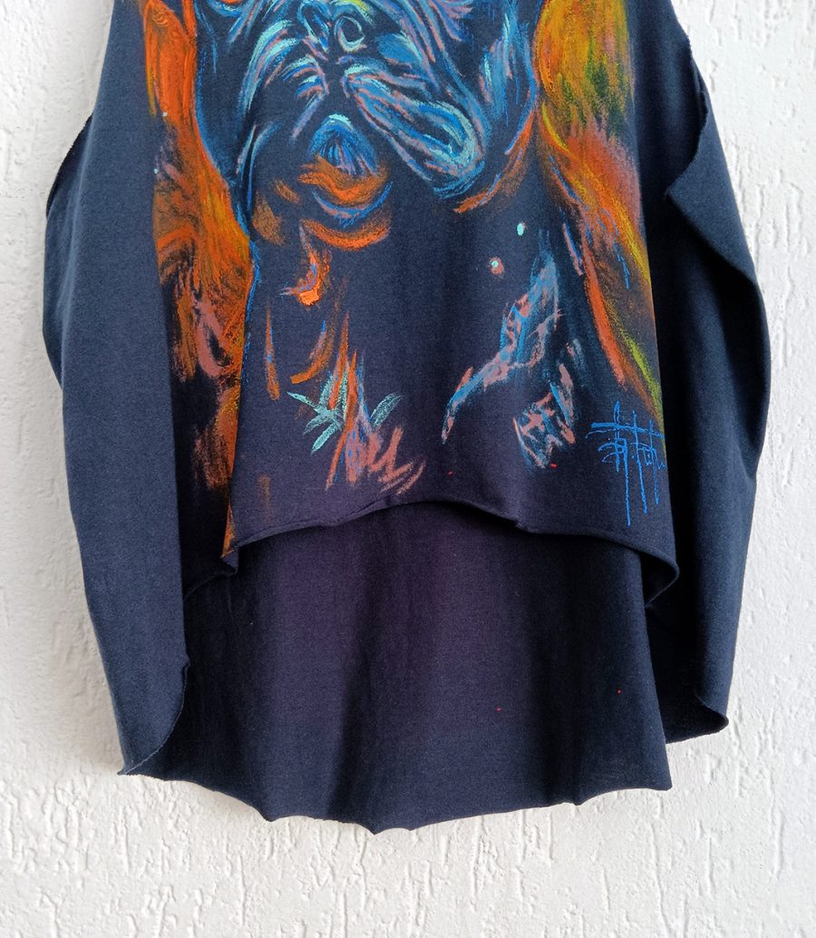 A close-up of the raw-edged bottom hem and the artist’s signature on the handcrafted tank top featuring orange, light blue and blue paintwork