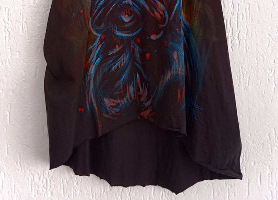 Dettaglio del bordo inferiore a taglio vivo e della firma dell'artista sulla canotta artigianale con pittura arancione azzurra e rossa