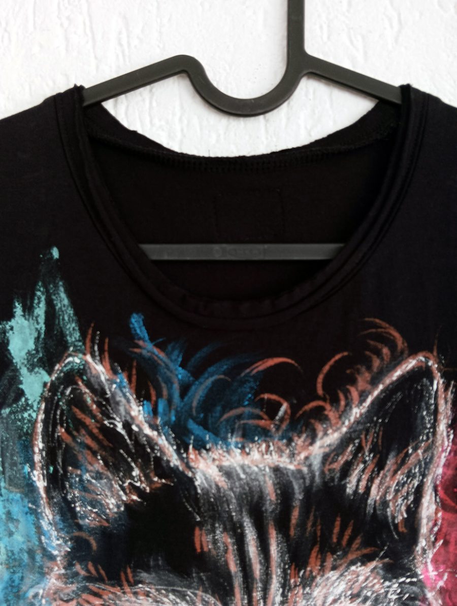 A close-up of the round neckline of the handmade black vest top, featuring light blue and red painted details on the upper part.