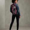 A vintage denim jacket with a hand-painted design on the back, worn by a model in a three-quarter profile pose